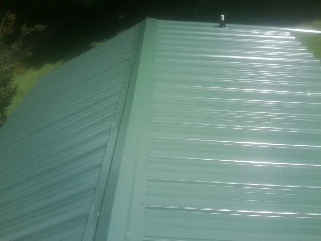 New green metal panels meeting at the ridge of a roof — Flat Roof Repair work by our crew in Erie